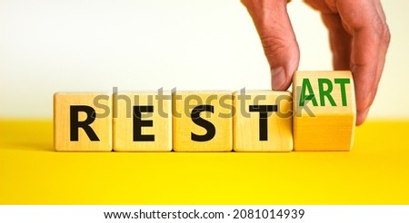 Rest and restart symbol. Businessman turns a wooden cube and changes the word rest to restart. Beautiful yellow table, white background, copy space. Business, rest and restart concept.