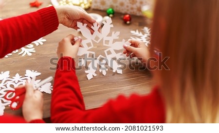 child with his mother carves snowflake for Christmas. family makes decorations for new year. Children's hands carve snowflake on background wooden table. Christmas theme. Selective focus. Rear view