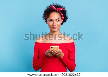Photo of sweet dreamy girl wear off-shoulders red shirt typing modern device looking empty space smiling isolated blue color background