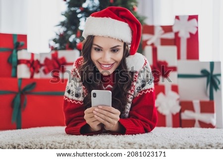 Full size photo of happy amazed cheerful young woman look phone lie floor santa claus indoors inside house home
