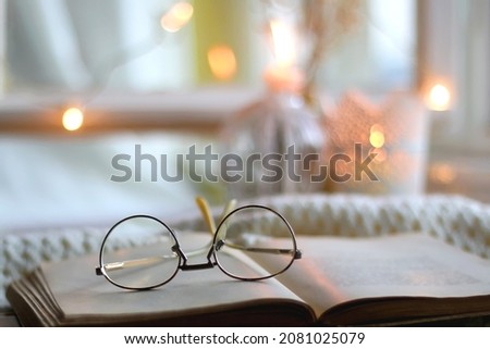 Open book and reading glasses. Candles and fairy lights in the background. Selective focus.