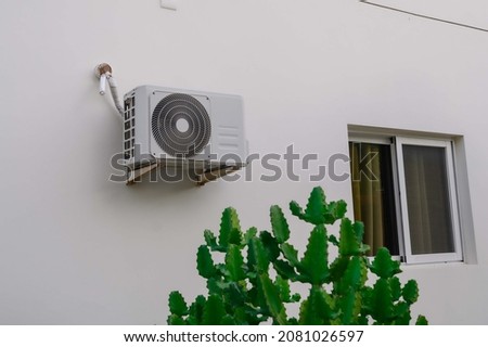 Air conditioner on white wall. Cactus on first plan. Photo HD with natural light. We can see window on right of air conditioner.
