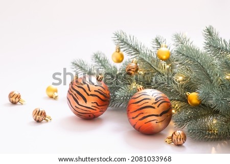 Christmas balls with hand drawn tiger stripes, decorative tree branch with garland. White studio background. Holiday card, idea for symbol of 2022, advertising, happy new year concept. Copy space.