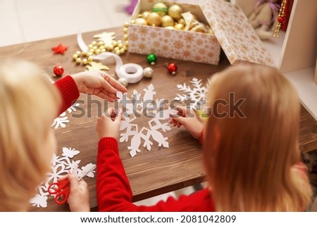 child with his mother carves snowflake for Christmas. family makes decorations for new year. Children's hands carve snowflake on background wooden table. Christmas theme. Selective focus. Rear view