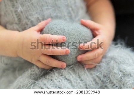 Close-up cute newborn's hands hold the gray hand made wool toy heart