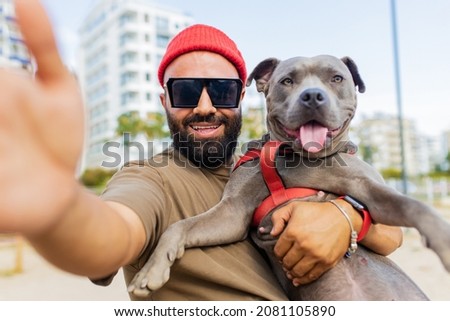 portrait of happy man in red hat and sunglasses with american terrier in dogs walking area park in city 