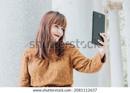 Young hipster red head woman having fun during a video call with the tablet.Day at the park, copy space, rest day. Beauty dress. Internet connection concept. Modern style during a sunny day.