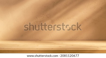 Empty table on bright brown wall background. Composition with leaves shadow on the wall and wooden desk. Mock up for presentation, branding products, cosmetics, food or jewellery.