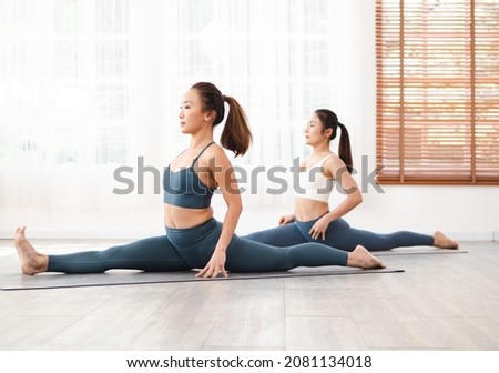 Yogi Asian women in Hanumanasana or front splits pose. Young female in sportswear practicing yoga, indoor work out on gym mat to stretches thighs, hamstrings, and groin, stimulates  abdominal organs.