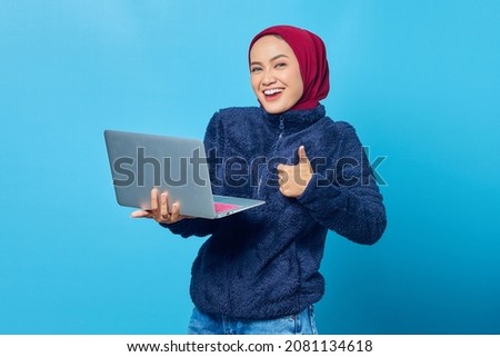 Beautiful asian woman using laptop smiling and showing thumbs up sign over blue background