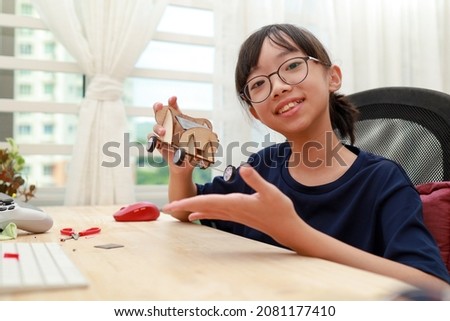 Teenage Asian girl building and showing her solar toy car through online e-learning at home. Student doing school project or learning science at home. Soft focus image.