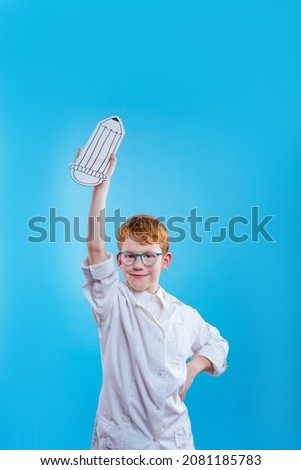Schoolboy wearing eye glasses and medical gown holding paper pencil sketch on blue background with blank space for text