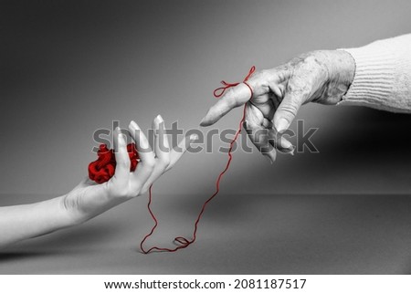 Hands of a young and an senior woman reach out to each other, connected by a red threads. Monochrome. The concept of Alzheimer's and Parkinson's disease. Royalty-Free Stock Photo #2081187517