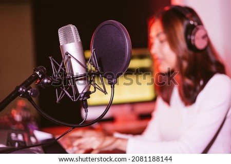 Studio microphone and pop shield on the mic in the empty recording studio with blur Asian woman in the background. Performance and show in the music business equipment.