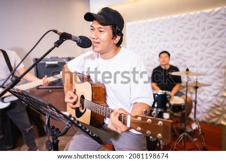 Handsome vocalist smiles for the camera while singing while playing acoustic guitar