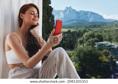 Attractive young woman use the phone looks at the screen in a comfortable hotel an open view of the Mountain View