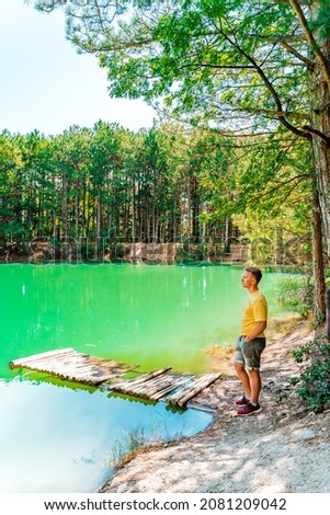 A blond man stands in front of an azure mountain lake in the forest in summer