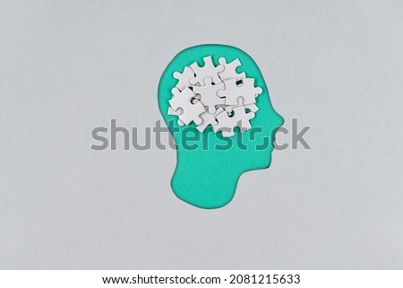 Cutout silhouette of a human cardboard head containing brain made from puzzle pieces, revealing thinking concept. Psychology
