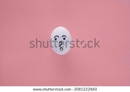 
One egg with painted emotions, on a light, red-pink, paper background. There is a questioning expression on his face, surprised, frightened. Copy space
