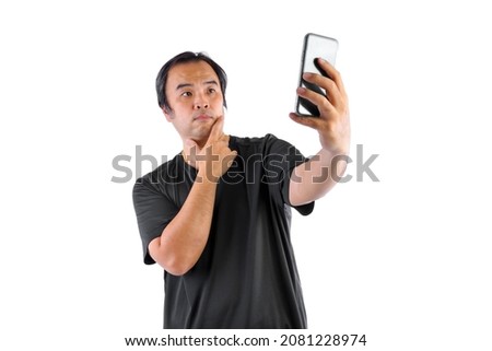 Asian man wore glasses and wear black t-shirts. Using mobile To take a picture  or selfie of himself isolated on blue background. 