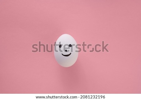 
One emoji egg with a smile on its face is set against a light red and pink paper background. Copy space. 