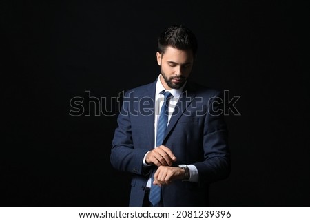 Handsome businessman looking at watch on dark background