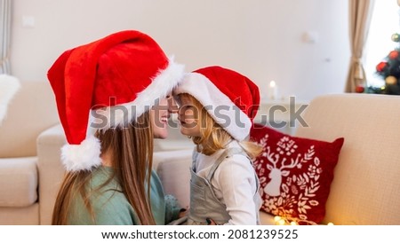 Happy daughter embracing her mother on New Year's day. Cheerful mom kissing cute baby daughter girl near Christmas tree. Merry Christmas and Happy Holidays. Mother and little child having fun 