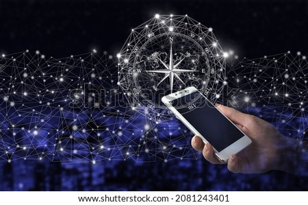 Navigation concept. Map and innovation concept. Hand hold white smartphone with digital hologram compass sign on city dark blurred background. Global network against a dark background