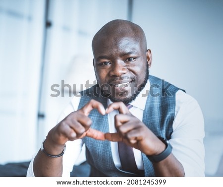 Romantic Office Manager Makes Heart of his Fingers and his eyes are Full of Love. Charming Guy Shows Heart-hand Symbol Close-up Portrait. Blurred Background. High quality photo