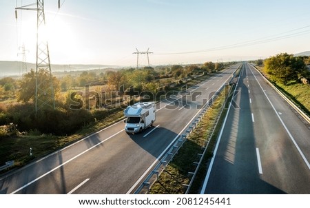 Camper car recreational vehicle with alcove driving along the rural countryside highway. Holidays and travel in motor home. Royalty-Free Stock Photo #2081245441