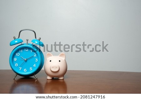 A picture of piggybank with clock on the table and copyspace. Saving and time value of money.