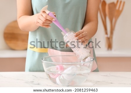 Woman cleaning baby bottle at home Royalty-Free Stock Photo #2081259463