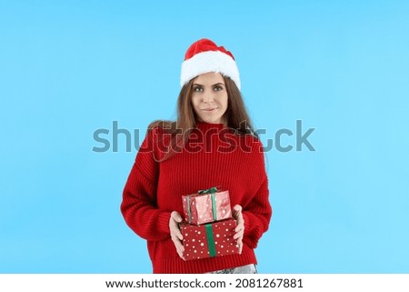Attractive woman in Santa hat holds gift boxes on blue background