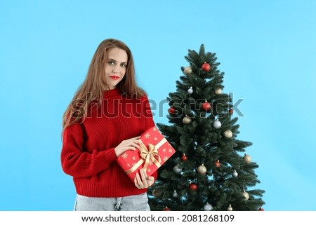 Attractive woman holds gift box on blue background with Christmas tree