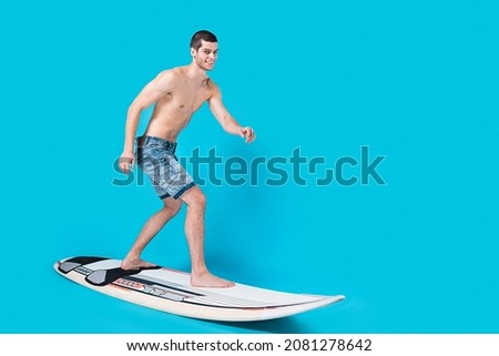 Athletic man riding a surfboard. Summer sport activity. Surfer movements on blue studio background.