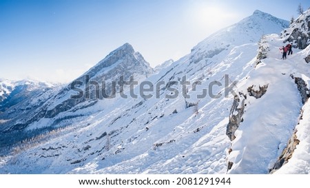 Group of four hikers with backpacks walks in mountains during winter day. There are mountains on the horizon.
