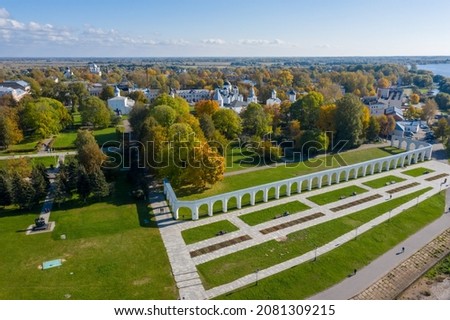 Panoramic aerial view of the Gostiny Dvor Arcade in Veliky Novgorod, autumn treetops on a sunny day. Remaining ruins of a medieval market. Monument to the heroes