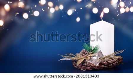 Blurred winter Christmas composition with one burning candle on Blue background with Light and Snow. New year concept with copy space.