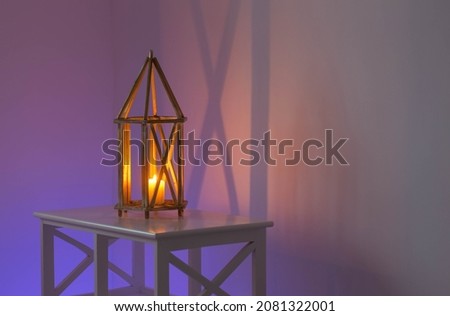 wooden lantern with burning candle on background of multi-colored illuminated wall
