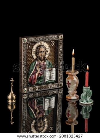The icon of the Lord Almighty made of solid oak on a black background with reflection and candles.