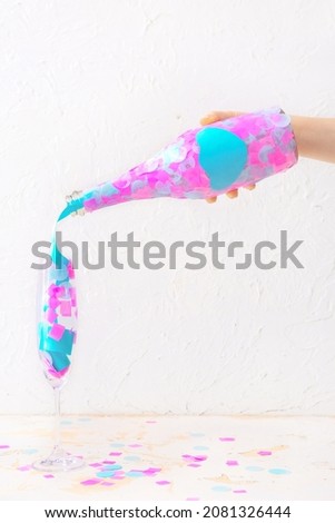 Female hand with bottle of champagne and glass with confetti on white background