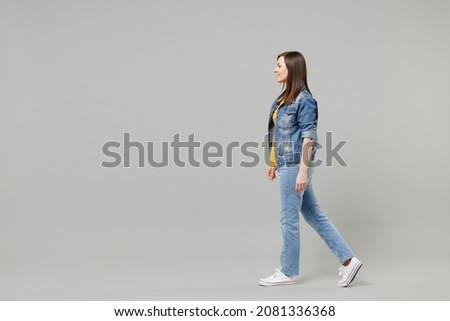 Full length side view young caucasian woman 20s wearing casual denim jacket yellow t-shirt looking aside walking going strolling isolated on grey background studio portrait People lifestyle concept Royalty-Free Stock Photo #2081336368