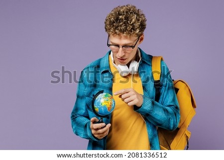 Young boy teen student in casual clothes backpack headphones glasses touch spin Earth world globe isolated on plain pastel violet background studio Education in high school university college concept