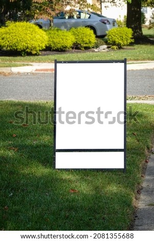 Blank white lawn sign with two panels on a green grass lawn near a sidewalk and street on a sunny day
