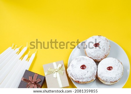 Happy Hanukkah. Jewish dessert Sufganiyot on yellow background. Symbols of religious Judaism holiday. Donuts, candles and gifts. Copy space.