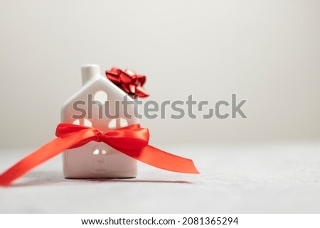 Christmas and New Year holiday. Miniature white toy house with red satin ribbon on white background. Flat lay, top view, copy space