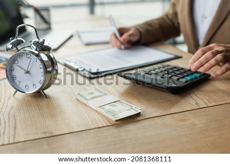 partial view of businessman signing contract near dollars, calculator and alarm clock, anti-corruption concept