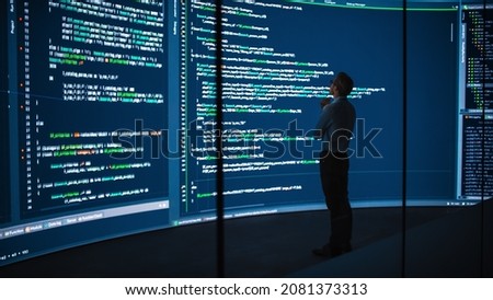 High-Tech Startup Concept: Innovative Male Software Engineer Standing, Doing Big Data Analysis on Wall Screen Showing Porgramming Code. Developing Futuristic e-Commerce App with Machine Learning. Royalty-Free Stock Photo #2081373313