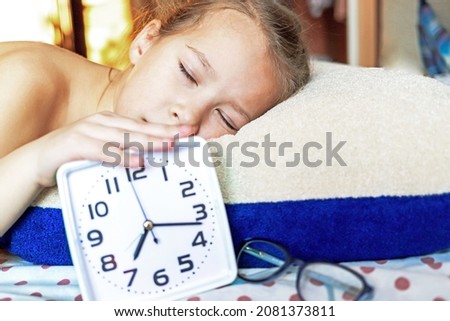 Girl sleeping on a pillow with an alarm clock in hand resting in the morning