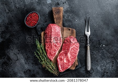 Fresh Raw Top Blade or flat iron beef meat steaks on a butcher cutting board. Black background. Top View Royalty-Free Stock Photo #2081378047